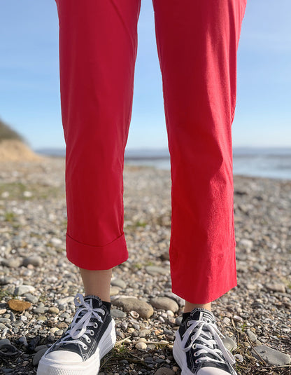 Person wearing red pants and black sneakers standing on a pebbly beach.