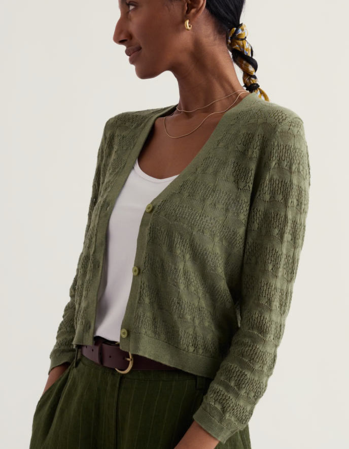 Woman wearing a green cardigan over a white top on a plain background