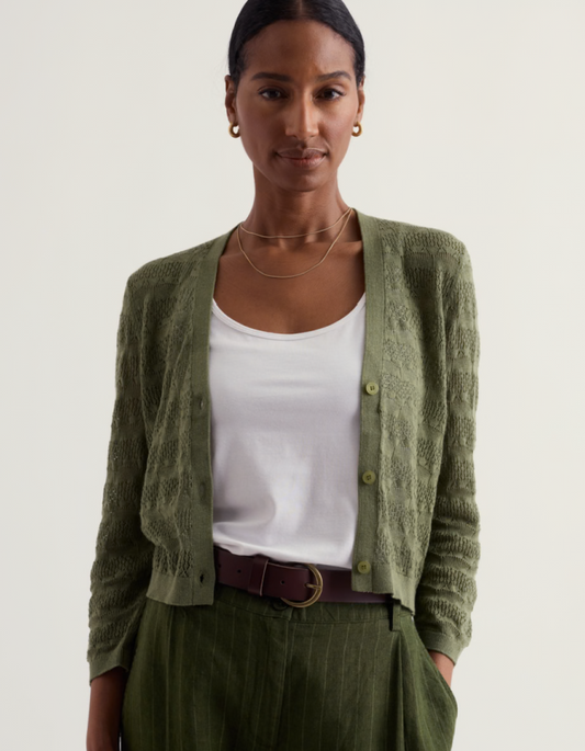 Woman wearing a green cardigan over a white shirt with a plain background