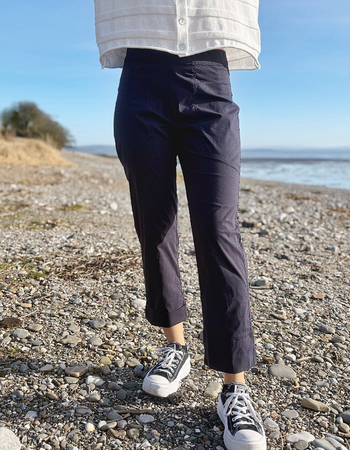 Person wearing navy pants and white sneakers on a pebbly beach.