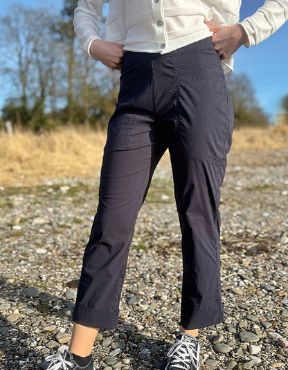 Person wearing navy pants and a white jacket standing on a gravel path with trees in the background.