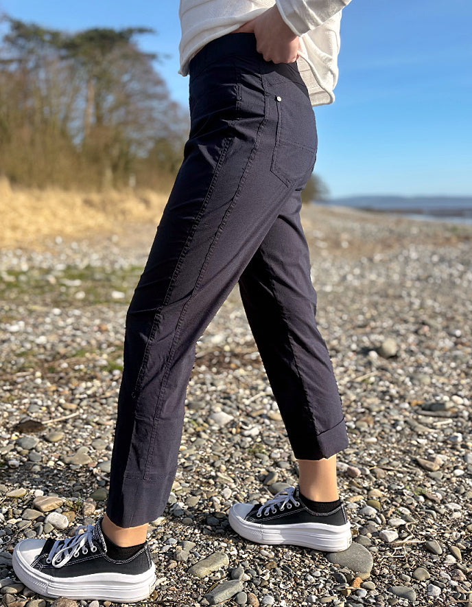 Person wearing navy pants and black sneakers standing on a pebbly beach.