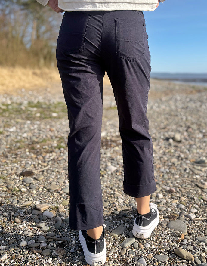 Person wearing navy pants standing on a pebbly beach with a blurred natural background