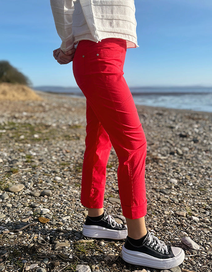Person wearing red pants and black sneakers standing on a pebbly beach with ocean in the background