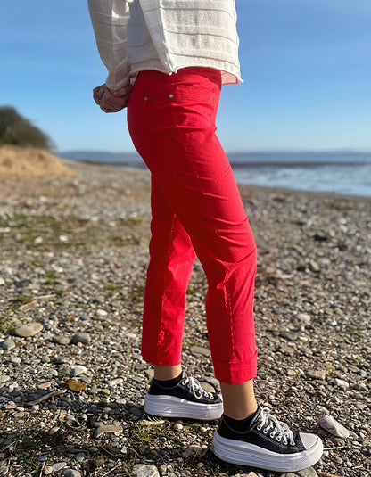 Person wearing red pants and black sneakers standing on a pebbly beach with ocean in the background