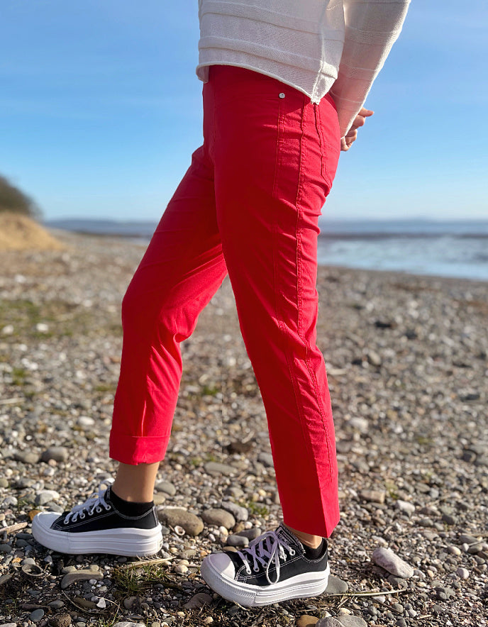 Person wearing red pants and black sneakers on a pebbly beach.