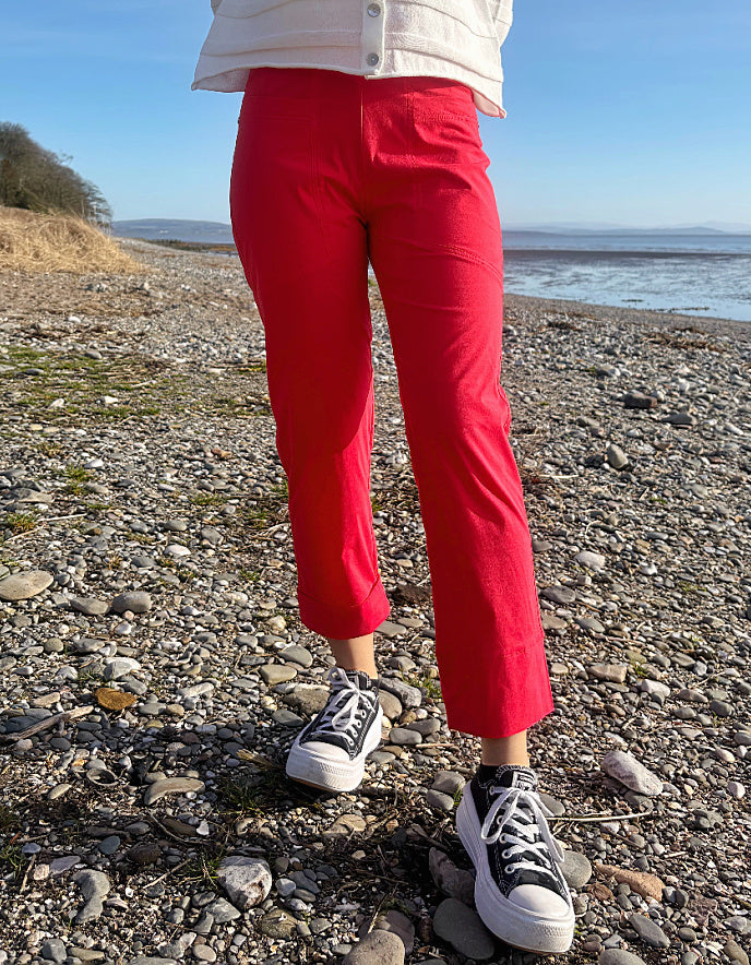 Person wearing red pants and black sneakers standing on a rocky beach.