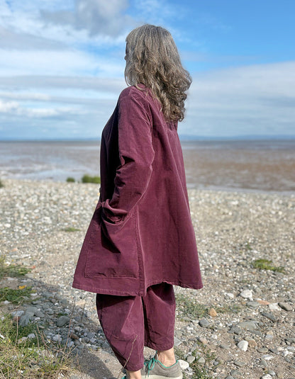 Person wearing a burgundy outfit standing on a pebbly beach with ocean and sky in the background