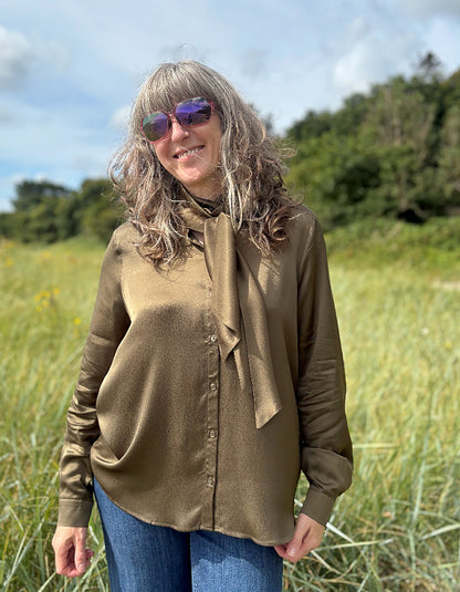 Person wearing a olive silky  blouse with a bow tie in a field