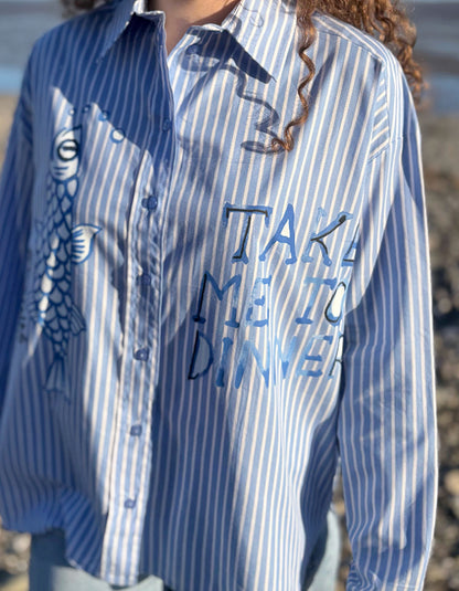 Blue and white striped shirt with text and graphic design worn by a person outdoors.