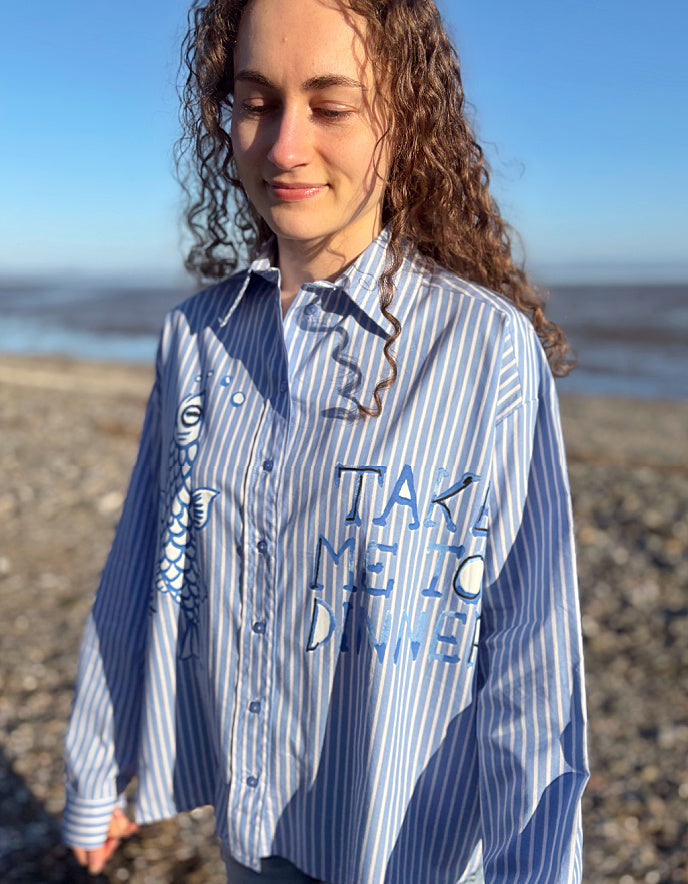 Person wearing a blue and white striped shirt with text on a beach
