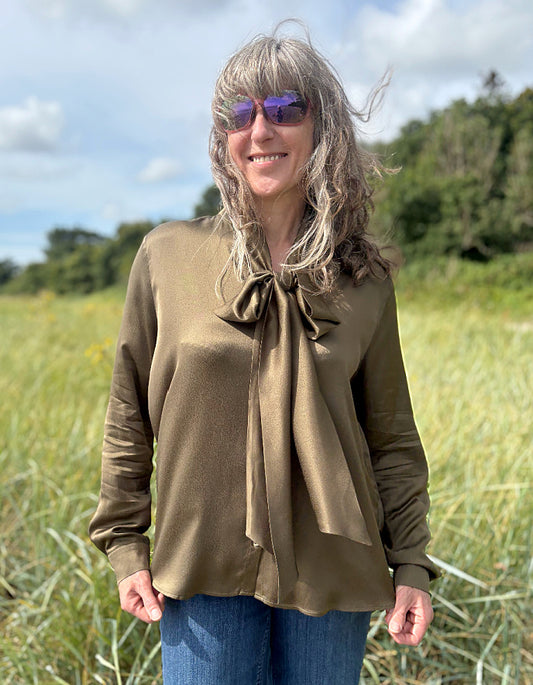 Person wearing a olive silky  blouse with a bow tie in a field