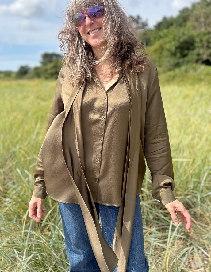 Person wearing a olive silky  blouse with a bow tie in a field