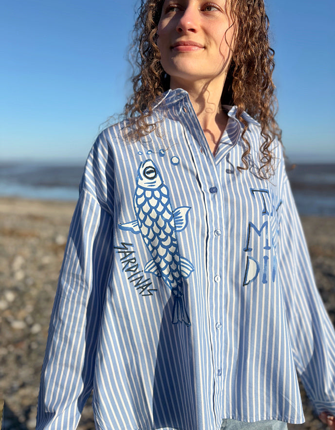 Woman wearing a blue and white striped shirt with a fish design outdoors.