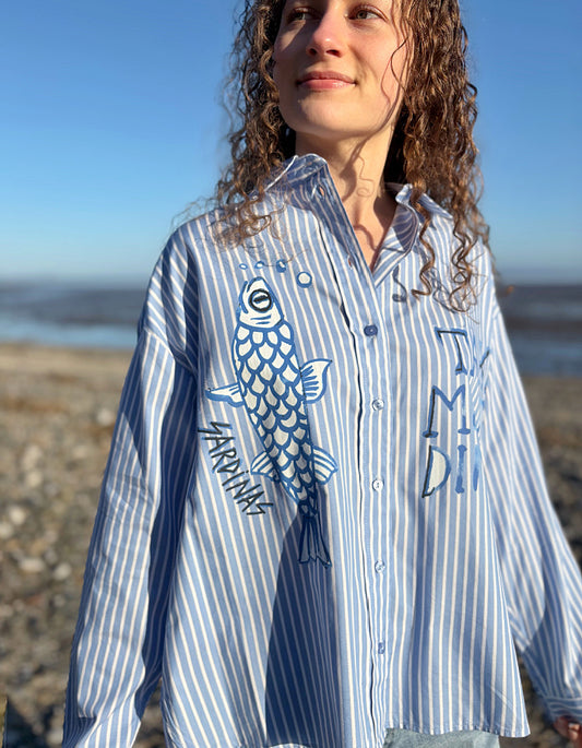 Woman wearing a blue and white striped shirt with a fish design outdoors.