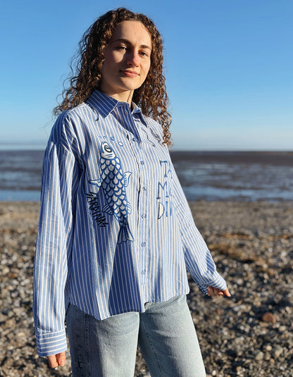 Woman wearing a blue and white striped shirt with a fish design on a beach