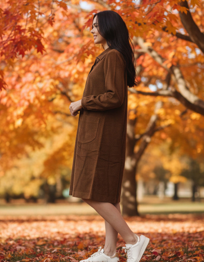 Woman in a brown cord dress standing in an autumn park with colourful leaves.