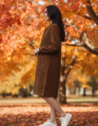 Woman in a brown cord dress standing in an autumn park with colourful leaves.