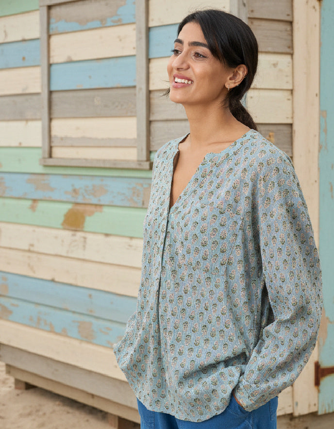 Woman wearing a light blue patterned blouse standing in front of a colorful wooden wall.