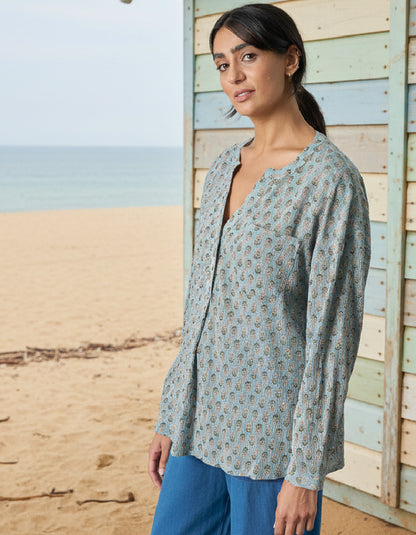 Woman wearing a light blue patterned shirt and blue pants standing on a beach.