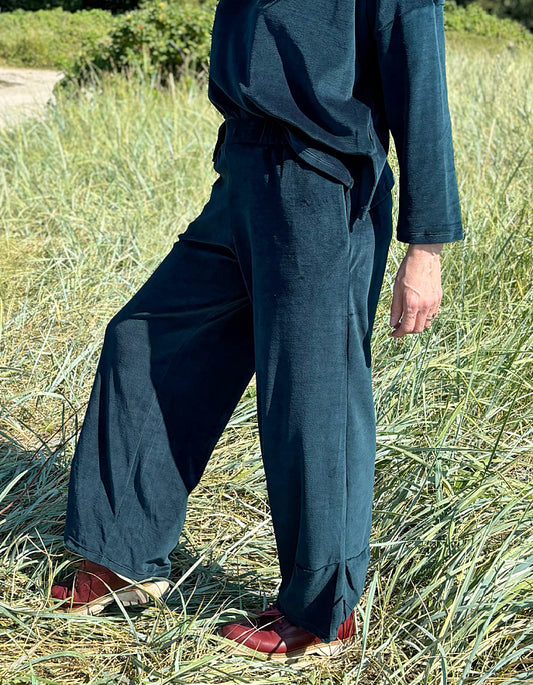Person wearing teal velvet pants and red shoes standing in a grassy field.
