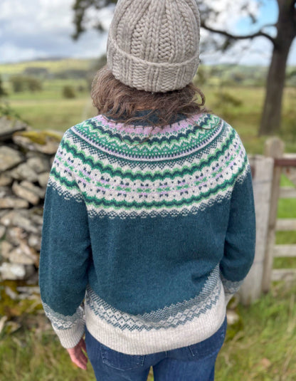 Person wearing a blue knitted sweater with a patterned design, standing outdoors in a natural setting.