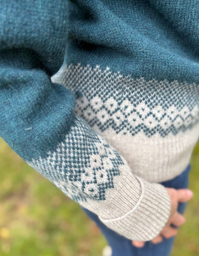 Close-up of a sweater with patterned cuffs and hem against a blurred natural background