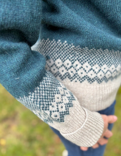 Close-up of a sweater with patterned cuffs and hem against a blurred natural background