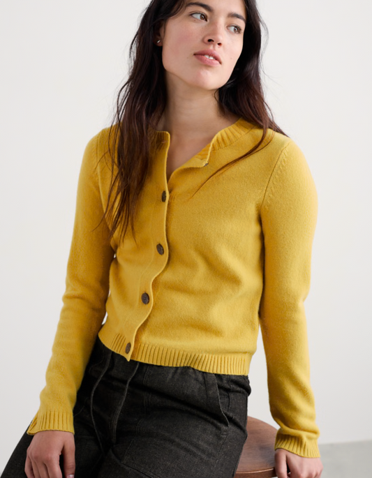Woman wearing a mustard yellow cardigan against a white background