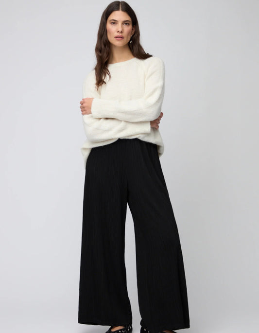 Woman wearing a white sweater and black pants on a plain background