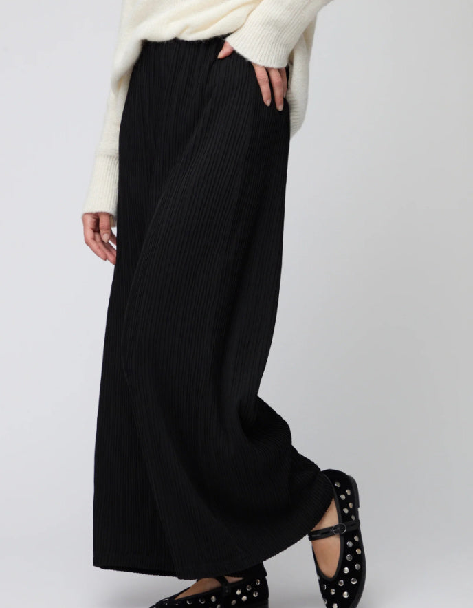 Person wearing a long black skirt with a white sweater on a plain background