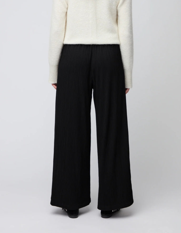 Person wearing black wide-leg pants and a white sweater on a plain background
