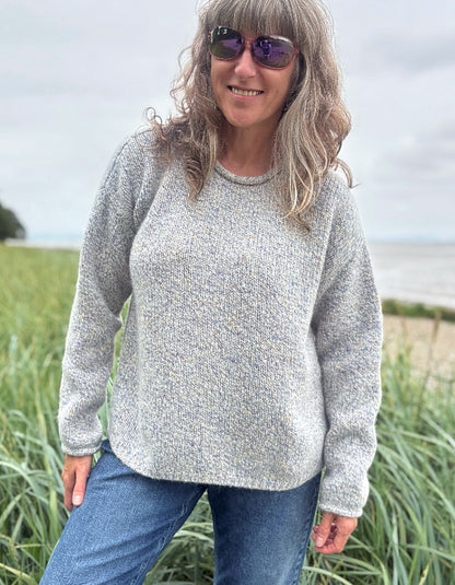 Person wearing a silver grey donegal tweed sweater and sunglasses standing in a grassy field with a cloudy sky.