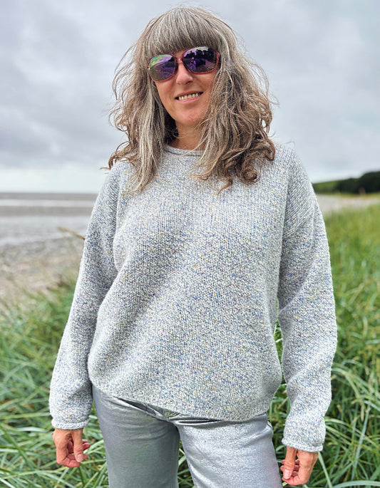 Person wearing a silver grey donegal tweed sweater and sunglasses standing in a grassy field with a cloudy sky.