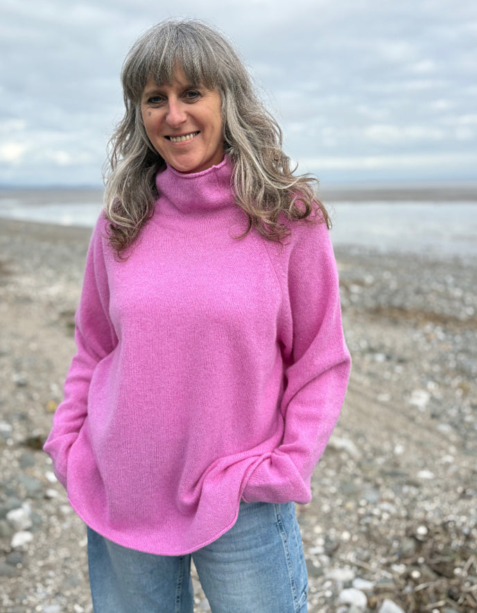 Woman wearing a pink wool merino sweater standing on a beach