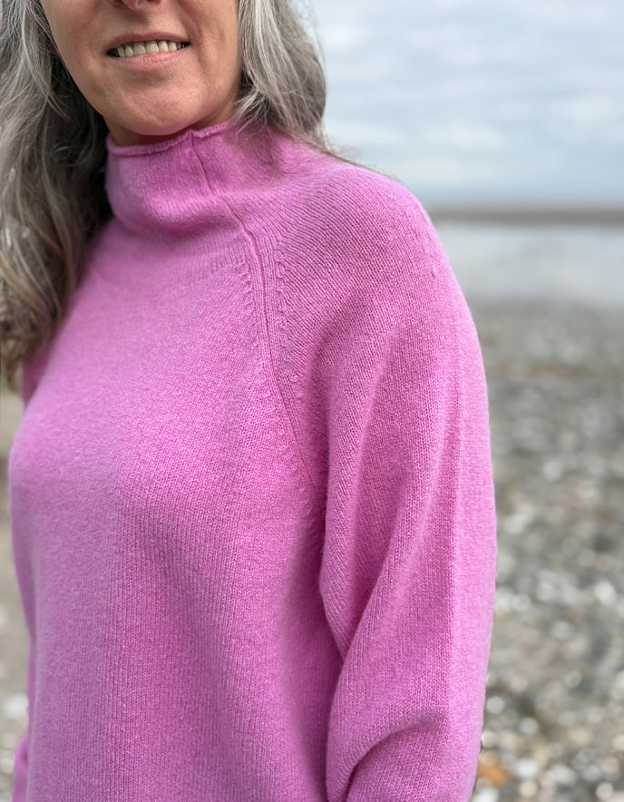 Woman wearing a pink wool merino sweater standing on a beach