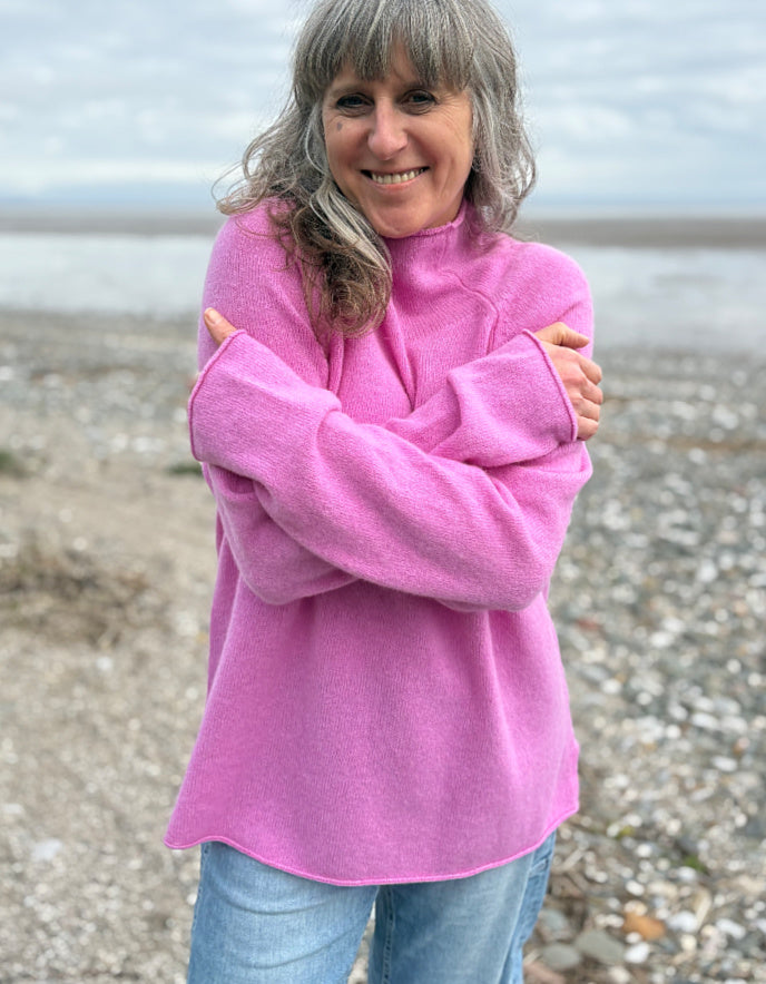 Woman wearing a pink wool merino sweater standing on a beach