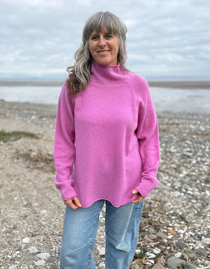 Woman wearing a pink wool merino sweater standing on a beach