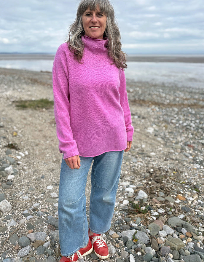 Woman wearing a pink wool merino sweater standing on a beach