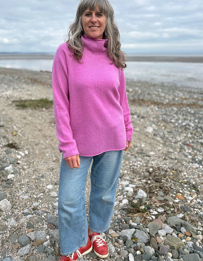 Woman wearing a pink wool merino sweater standing on a beach