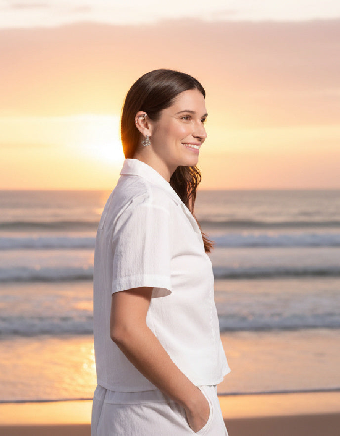 Woman in a white outfit standing on a beach at sunset