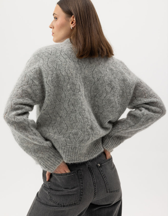 Person wearing a gray cable knit sweater on a white background