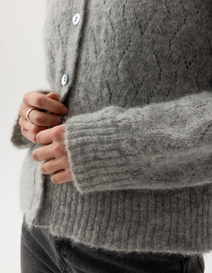 Close-up of a person wearing a gray cable knit cardigan with a white background