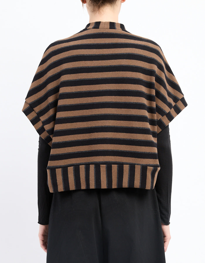 A person shown from the back wearing a brown and black horizontally striped knit poncho-style cardigan over a black long-sleeve top and black skirt, against a plain white studio background.