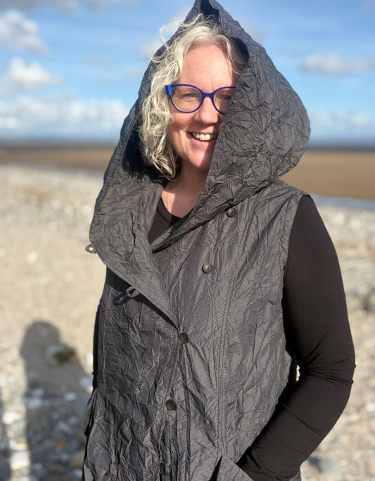 Person wearing a gray quilted vest on a beach with a blue sky.