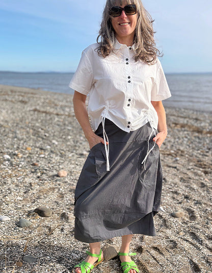Woman standing on a beach wearing a white blouse and gray skirt.