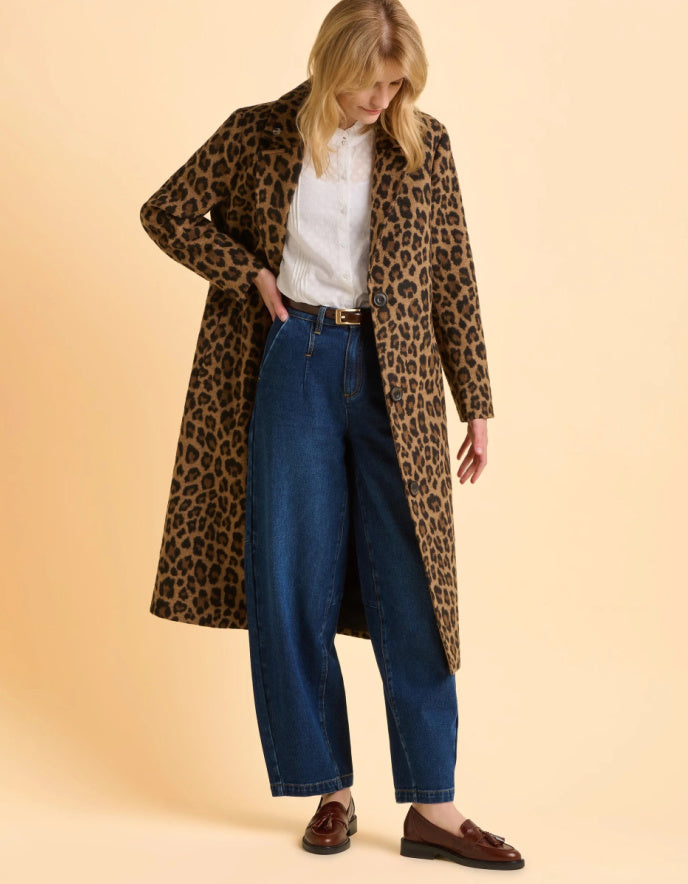 Woman wearing a leopard print coat, white shirt, blue jeans, and brown shoes on a beige background