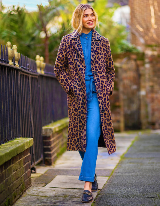 Person wearing a leopard print coat and blue jeans walking on a sidewalk.
