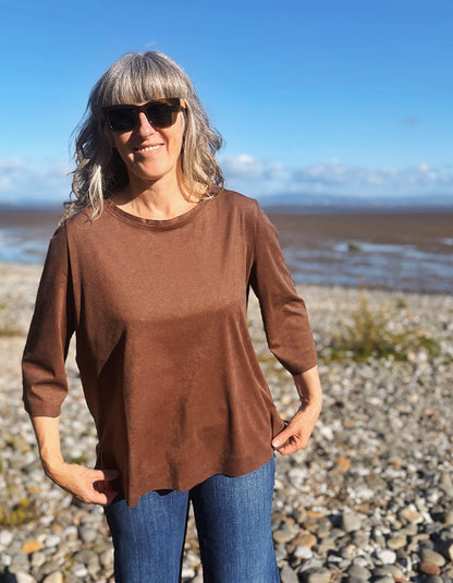 woman wearing vegan suede brown boxy t shirt with 3/4 length sleeves with jeans on a beach