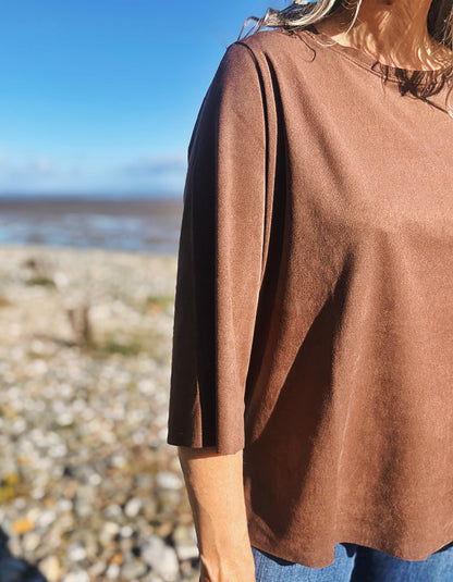 woman wearing vegan suede brown boxy t shirt with 3/4 length sleeves with jeans on a beach